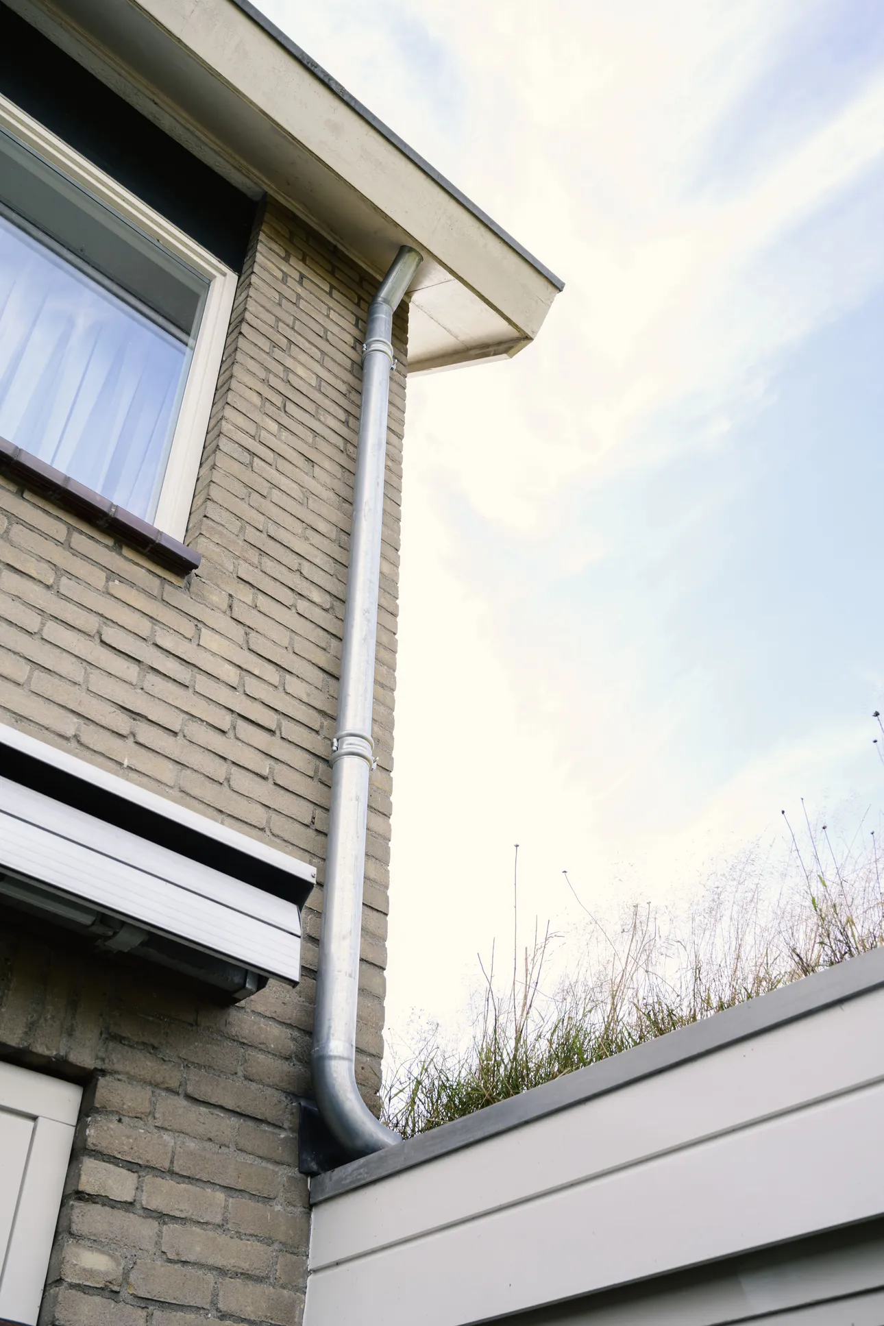 Regenpijp komt uit op het groenblauwe dak