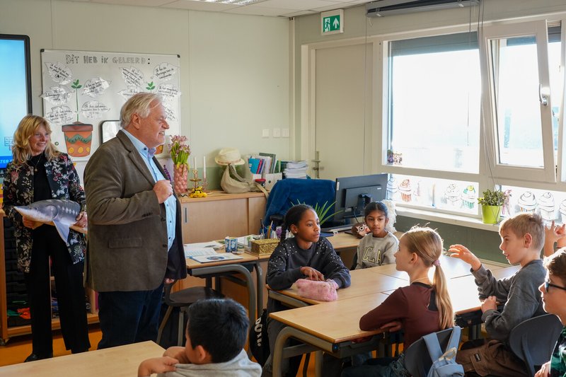 Een hoogheemraad legt wat uit aan kinderen in het klaslokaal